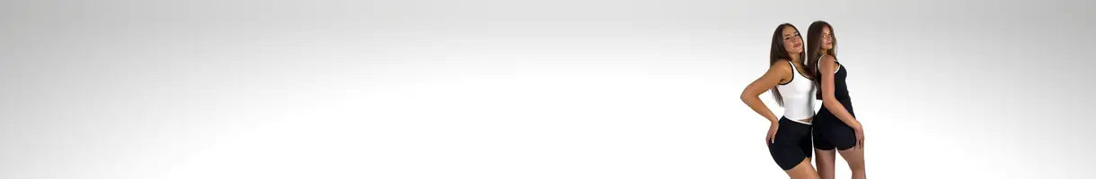 Dwie kobiety w pasujących czarnych szortach i białych bluzkach stoją obok siebie na tle jednolitego tła.